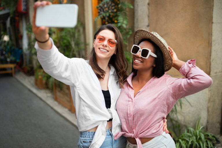 Smiling millennial african american and caucasian ladies tourists in hat and sunglasses taking